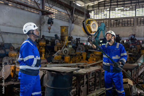 Diverse team of engineers worker using overhead crane hoist to carry raw materials inside metal sheet manufacturing factory for heavy industry usage