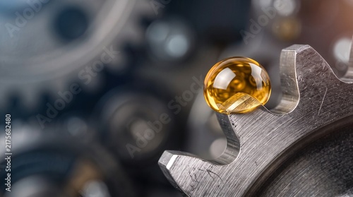 A single drop of golden lubricant on a metallic gear in a machine