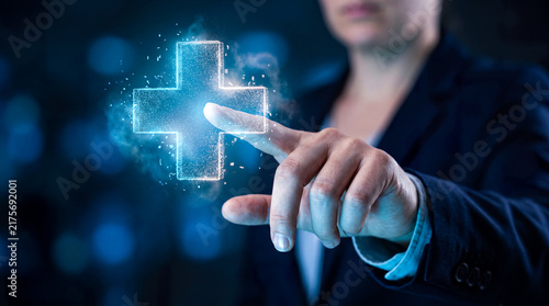 Digital medical cross hologram button glowing blue light particles touched by business professional for health care technology.