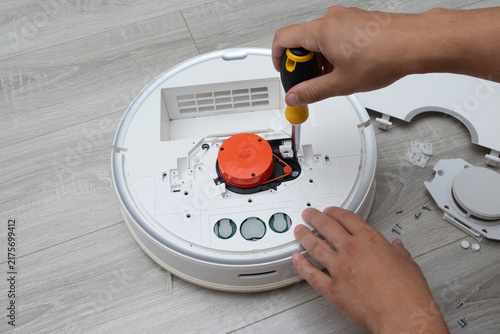 Technician loosening a screw while working on the internal mechanism of a disassembled robot vacuum cleaner. Concept of vacuum cleaner repair, appliance maintenance, electronics servicing