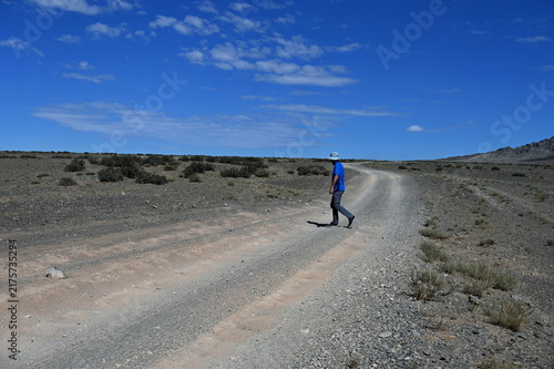 Senior hiker walking across the gravel road in Gobi Desert