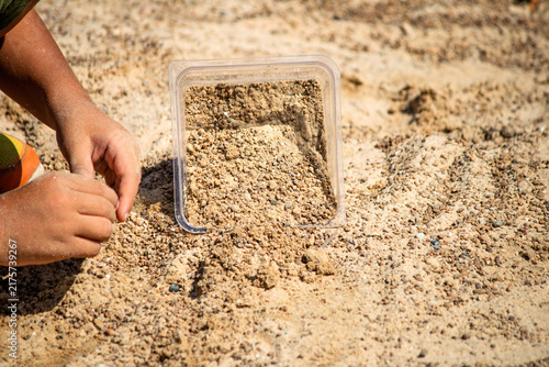 The kid, whose hands are visible, is playing with sand. Children's playground or sandbox. Outdoor children's activity. Horizontal photo.