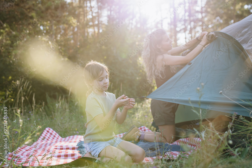 Naklejka premium Girl and mom setting up tent together during summer camping trip.