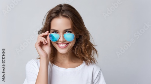 Young woman smiling while wearing blue sunglasses in studio