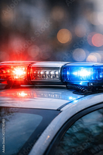 Nighttime police car with flashing red and blue lights. Emergency lights glow brightly on roof of patrol vehicle. Blurry background highlights the vivid light display