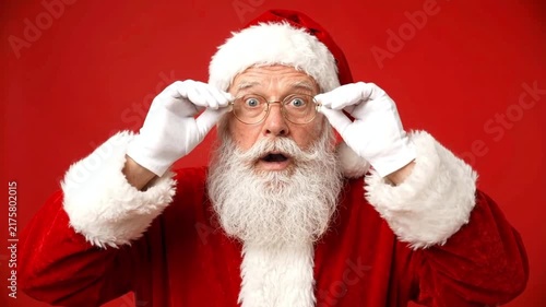 Surprised Santa Claus Adjusting Glasses on Red Background, Funny Christmas Studio