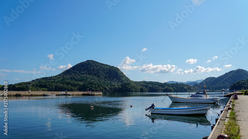Fototapeta 澄み切った青空と山影を映し出す静かな水面に浮かぶ小さな漁船