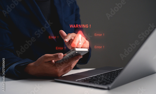 Person experiencing smartphone error with warning messages displayed, sitting at desk with laptop