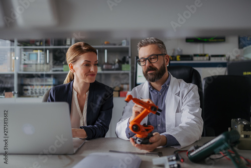 Robotics engineers working on laptop and desinging modern robotic arm in laboratory.