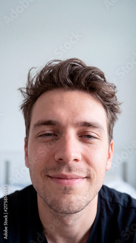 Genuine young man gazes calmly at the camera in soft natural window light