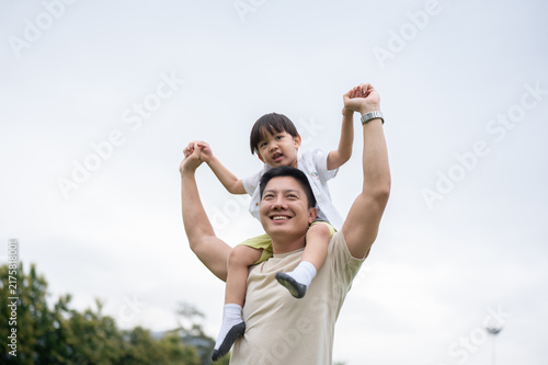 Принти на полотні Asian father giving his young kid son shoulders ride during family playtime in park under clear sky