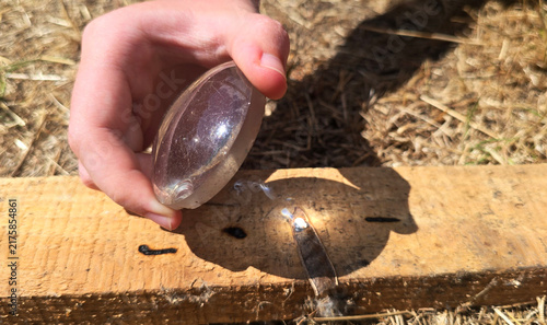 Teenager's hand focusing sunlight through a glass lens to burn wood with visible smoke