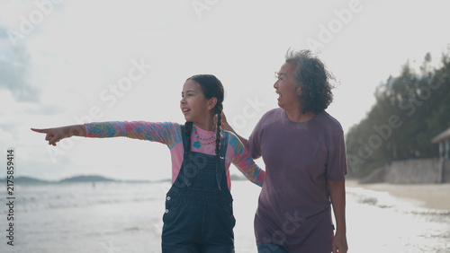Obraz na plátně A young girl points toward the horizon while walking on the beach with her smili