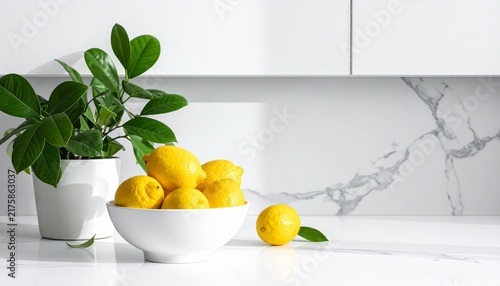 Fresh vibrant yellow lemons in a white bowl placed on a modern marble kitchen countertop next to a small green houseplant in interior decor.