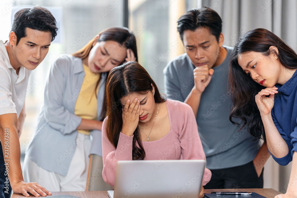 Fototapeta premium Stressed young asian business team dealing with work pressure, conflict and difficult problems together around laptop in office