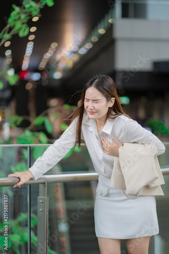 Bild auf Leinwand Chest pain concept of a young businesswoman clutching her chest and holding a railing for support at work, showing sudden discomfort