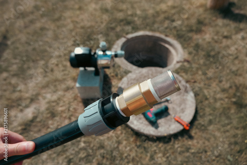 фотографія Hand holding black HDPE pipe with brass check valve and mesh strainer in front o
