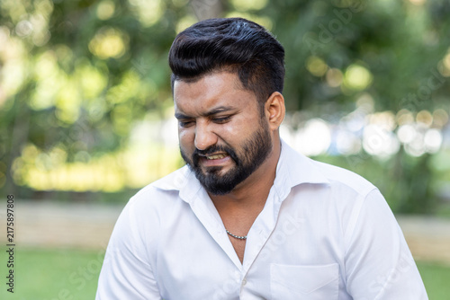 south asian man in his 20s with pained and distressed face, outdoor scene