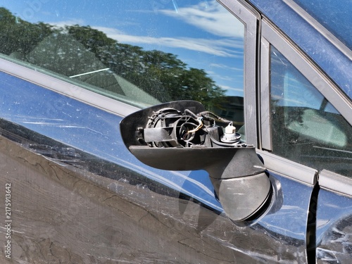 Фотография Broken side mirror of a black car showing exposed internal wires and damaged casing after a traffic accident in daylight