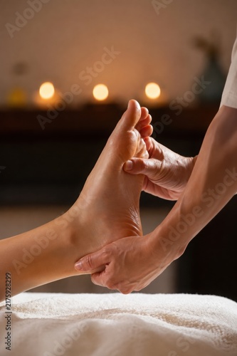 Professional foot massage with therapist hands gently stretching and supporting the client's foot in a luxury spa setting with warm candlelight, relaxing wellness atmosphere and therapeutic care