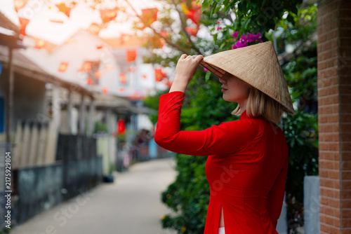 Bild auf Leinwand Caucasian woman in red ao dai with traditional hat in hoi an, vietnam street lif