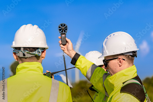 Obraz na płótnie Handheld anemometer held aloft between two workers in yellow coveralls, the impe