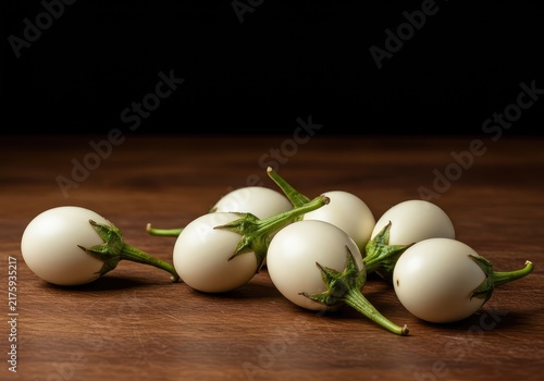 Cluster of small, glossy, white eggplant fruits resting on a wooden table, resembling large white eggs, symbolizing new growth and harvest ,solanum ,farming ,raw