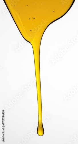 Golden colored liquid oil dripping down slowly onto a perfectly isolated pure white surface in a studio setting. This clear viscous material is healthy ,essential ,energy ,food