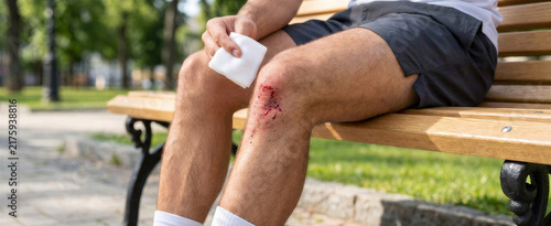 Man cleaning deep abrasion on knee while sitting on a park bench  
