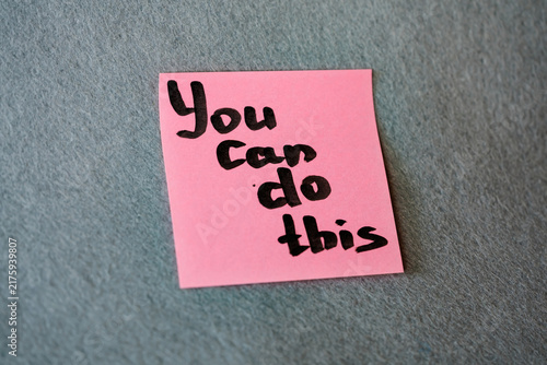 Pink sticky note with handwritten motivational phrase Yes You Can on grey felt background, motivation concept