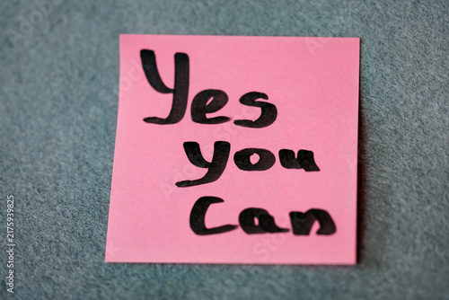 Pink sticky note with handwritten motivational phrase Yes You Can on grey felt background, motivation concept