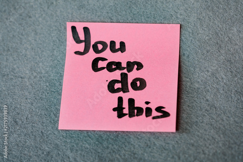 Pink sticky note with handwritten motivational phrase Yes You Can on grey felt background, motivation concept