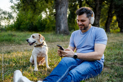 Konstfotografi Man sitting on grass with dog while using smartphone in park