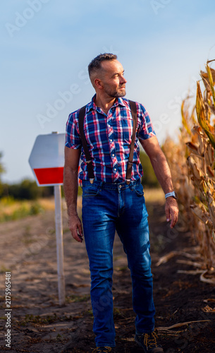 Full length portrait of farmer walking by ripe corn field looking away.