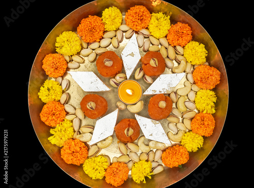 Foto Traditional Indian festival Diwali pooja thali with sweets and oil lamps on dark background, gold plated featuring colorful marigold flower, cashew nuts, laduoo, and kaju katli sweets decorations