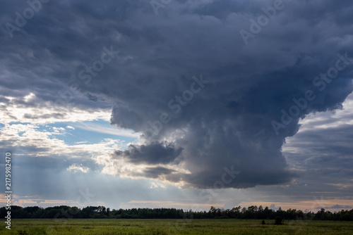 Massive storm cloud formation over green field with sunbeams breaking through, dramatic sky