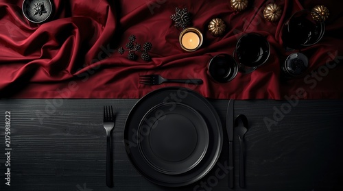 Against the background of the flowing dark red fabric, an elegant table setting is presented with black matte dishes, glasses and cutlery to match the tone on a dark wooden surface.