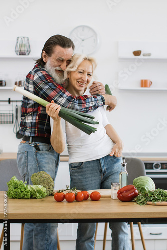 Canvastavla An elderly couple embraces in a bright kitchen, surrounded by fresh vegetables,