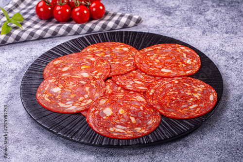 Obraz na płótnie Spicy chorizo salami slices on black plate with fresh cherry tomatoes and basil