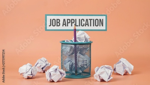 Rejected job application papers in a trash bin with sign