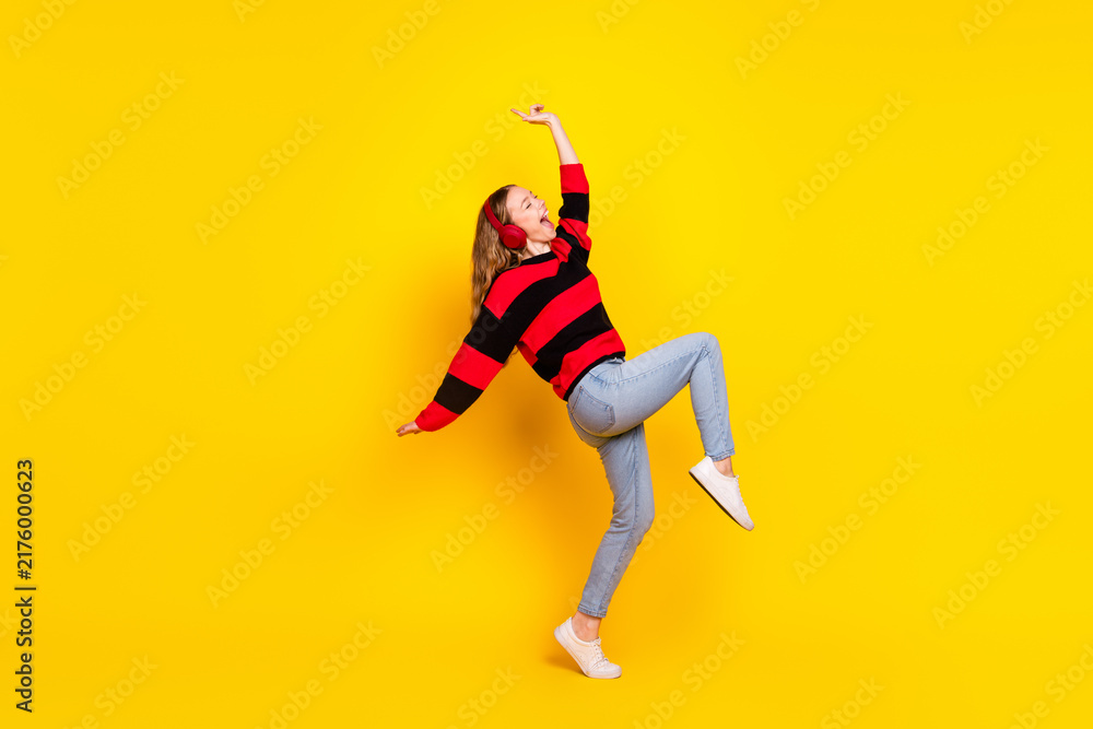 Fototapeta premium Cheerful young woman in a striped sweater posing energetically against a bright yellow background showcasing stylish casual fashion.