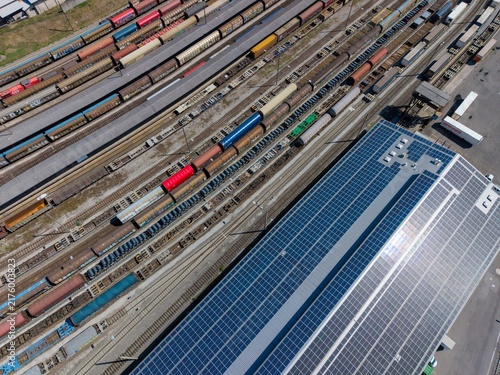 Aerial view of Chiasso Cargo Train Terminal with numerous freight trains on tracks and a large warehouse roof covered in solar panels in Chiasso, Ticino, Switzerland.
