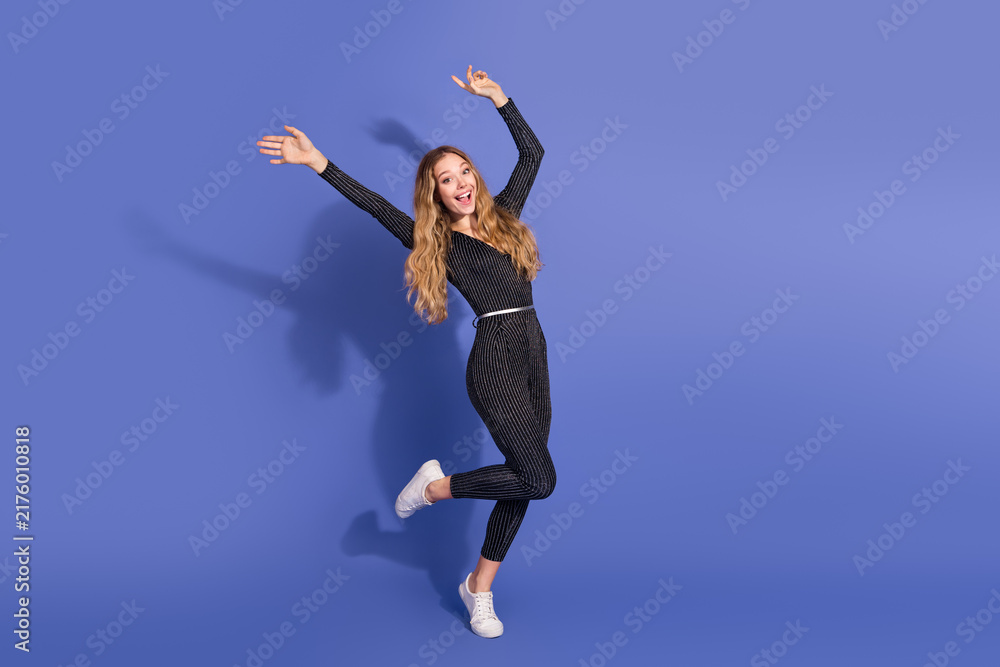 Fototapeta premium Young woman in striped jumpsuit leaps with joy against blue background showcasing playful fashion and lifestyle moment