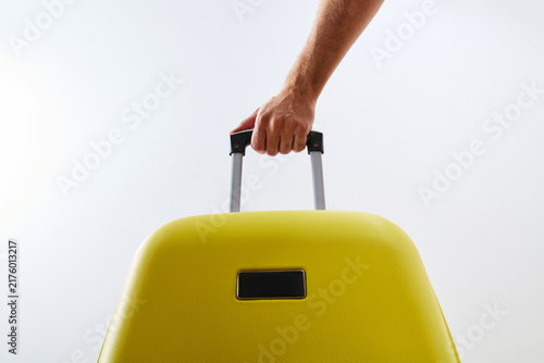 Foto Hand of Traveler Holding Handle of Yellow Suitcase on Light Background