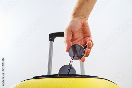 Foto Man Hand Holding Sunglasses Over Yellow Travel Suitcase