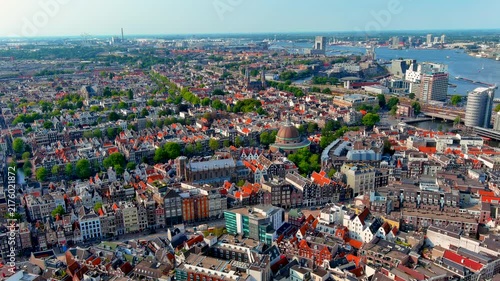 Aerial drone view over the rooftops of the Amsterdam historic center with the Koepelkerk dome, Nieuwe Kerk, canal houses, the IJ river and the western harbor, Netherlands, in summer.