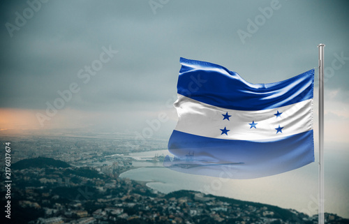 Foto Honduras flag waving over a coastal city under dramatic cloudy sky, realistic fabric motion, aerial seaside landscape background