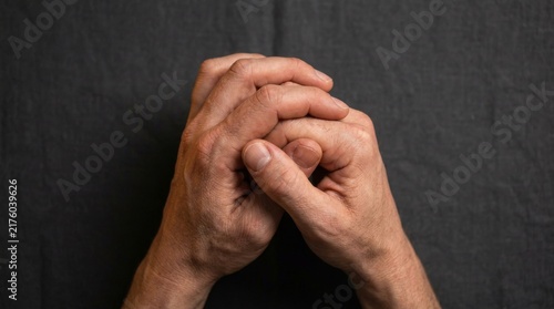 Clasped male hands resting on dark gray textile surface representing prayer or meditation