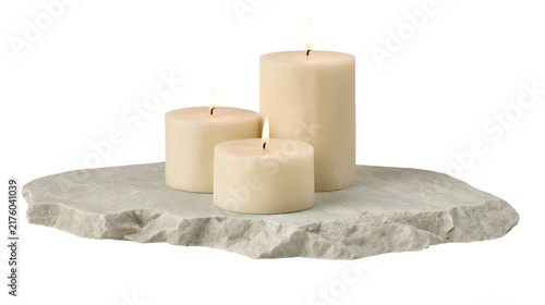 Bild auf Leinwand Three cream pillar candles burning on a rough grey stone slab, isolated on trans