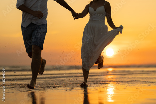 Couple walks hand in hand on the beach during sunset with waves and reflections in the sand